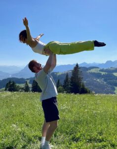 Junger Mann hebt junge Frau vor Bergpanorama